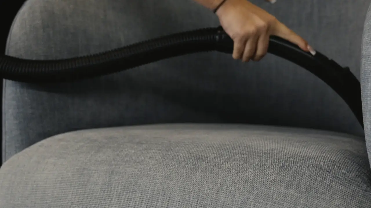 A Castle Cleans cleaner running a vacuum attachment over a grey upholstered office chair